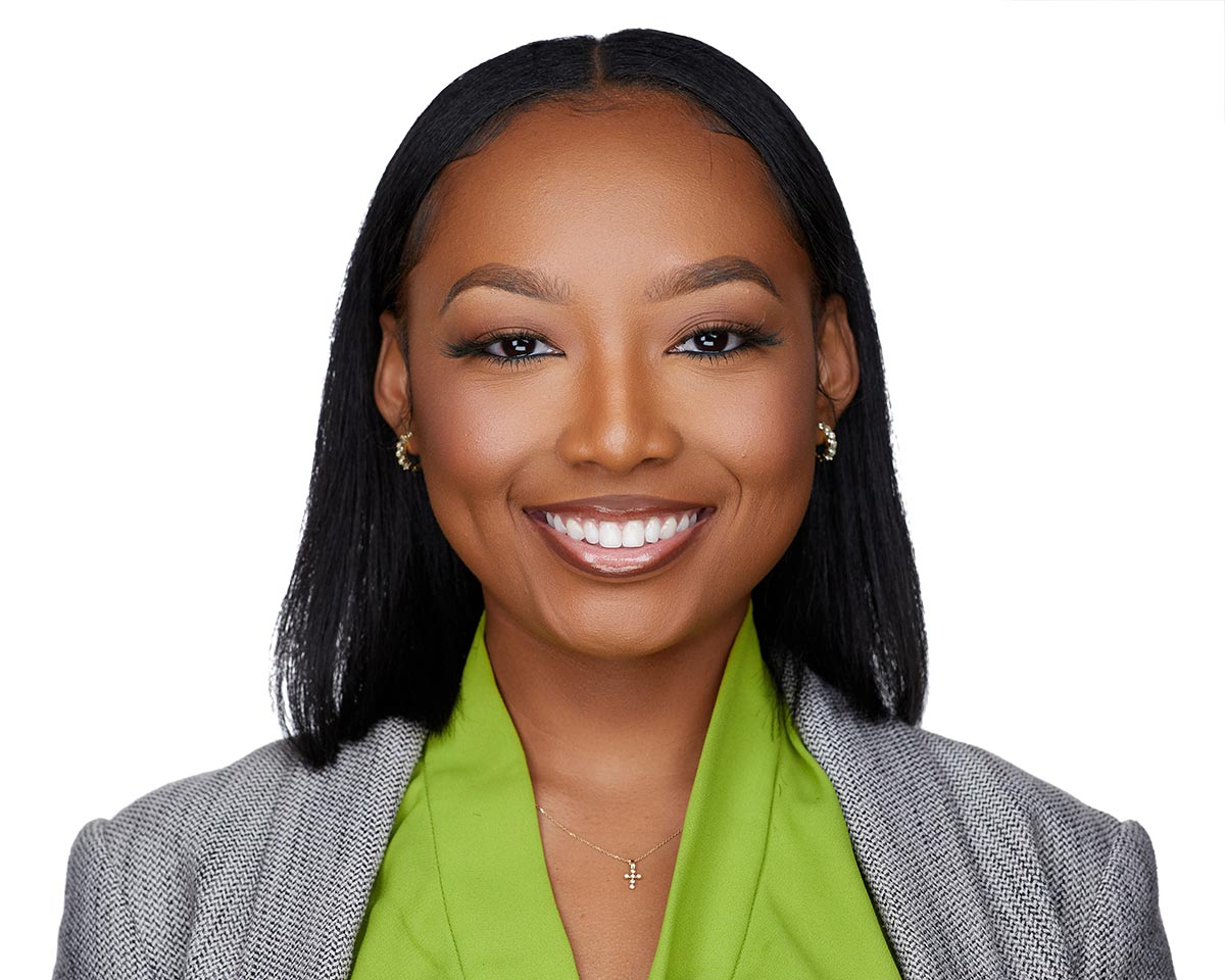 Professional black female lawyer headshot in Los Angeles wearing a gray jacket suite with a green blouse and smiling on a white background