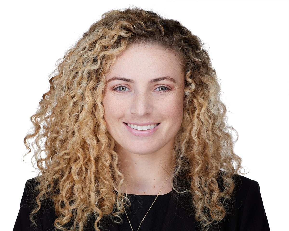 Professional white female lawyer headshot in Los Angeles with a blond curly hair wearing a black jacket suite with a black blouse and smiling on a white background