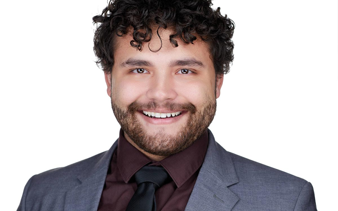 Professional white male lawyer headshot in Los Angeles with a curly black hair wearing a gray jacket suite and a brown shirt and black tie smiling on a white background