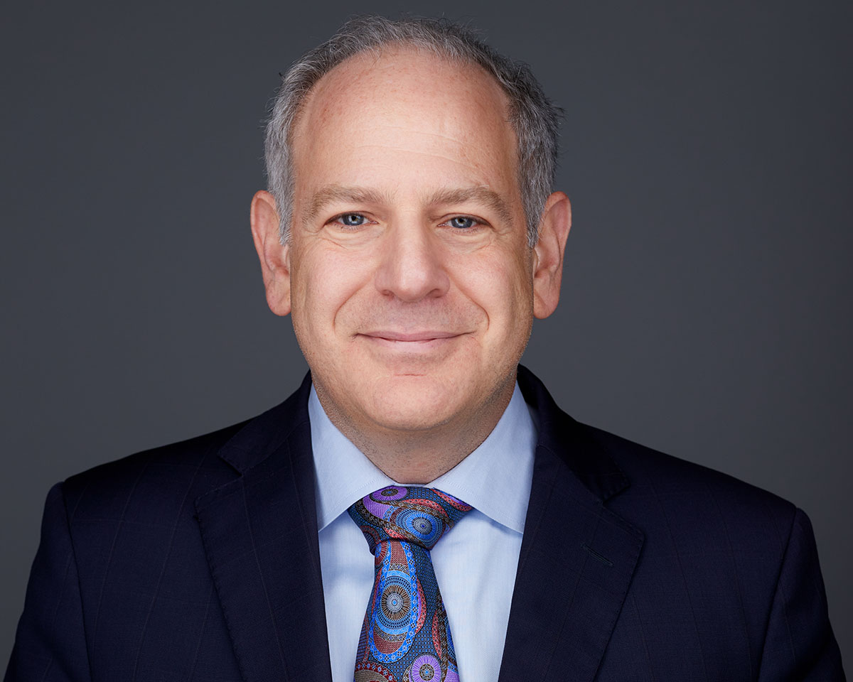 Professional white male executive headshot in Los Angeles wearing a navy jacket suite with a blue shirt and colorful tie and smiling